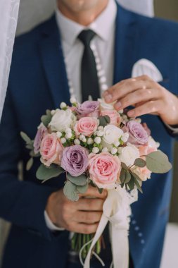 Mavi takım elbiseli bir adam elinde bir buket çiçek tutuyor. Buket pembe ve beyaz çiçeklerin karışımıdır.
