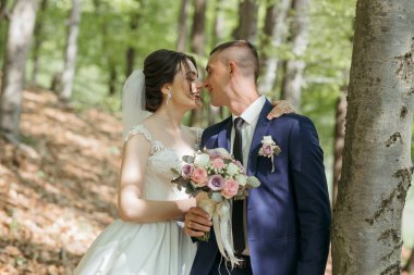 Gelin ve damat bir ormanda duruyorlar, gelin bir buket tutuyor ve damat bir buket tutuyor.