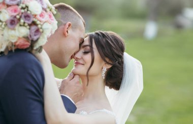 Bir gelin ve damat bir tarlada birbirlerini kucaklıyor. Gelin beyaz bir elbise ve duvak takıyor. Sahne romantik ve samimi.