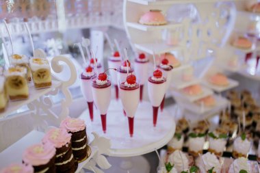 Kekler, kekler ve dondurma dahil çeşitli tatlılarla dolu bir tatlı masası. Tatlılar görsel olarak çekici bir şekilde düzenlenir ve bazıları pembe renk düzenine sahiptir.