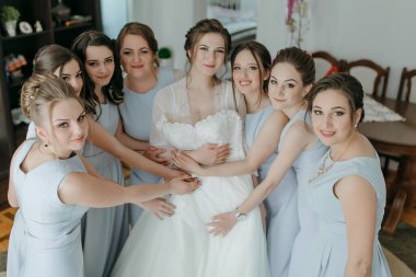 Bir gelin, grup fotoğrafında nedimeleriyle çevrilidir. Gelin beyaz bir elbise giyiyor ve nedimeler mavi elbiseler giyiyor. Gelin olarak sahne neşeli ve kutlayıcıdır.