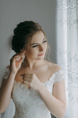 Bir kadın düğünü için hazırlanıyor ve küpelerini takıyor. Yüzünde bir gülümsemeyle kameraya bakıyor.