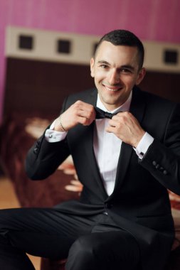 Takım elbiseli bir adam kravatını bağlamaya hazırlanıyor. Gülümsüyor ve keyfi yerinde.