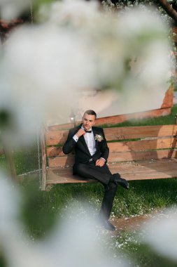 Takım elbiseli bir adam bankta kucağında çiçekle oturuyor. İmajın romantik ve samimi bir havası var.