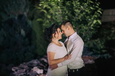 Bir çift karanlıkta sarılıyor. Adam beyaz bir gömlek giyiyor ve kadın beyaz bir elbise giyiyor.