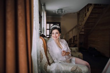 Beyaz elbiseli bir kadın bir odada sandalyede oturuyor. Gülümsüyor ve pencereden dışarı bakıyor.