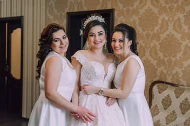 Üç kadın fotoğraf için poz veriyor, biri gelinlik giyiyor. Sahne mutlu ve kutlama dolu.