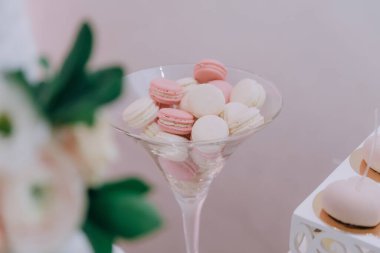 Pembe ve beyaz makaronlarla dolu bir cam kase. Makaronlar martini bardağındaymış gibi görünecek şekilde dizilmişler. Kase bir vazo çiçeğin yanındaki masaya konur.