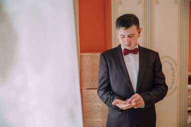Takım elbiseli ve kırmızı papyonlu bir adam elinde bir yüzük tutuyor. Adam takım elbise ve kravat giydiği için resmiyet ve zarafet kavramı. Elinde tuttuğu yüzük özel bir durum olduğunu gösteriyor.