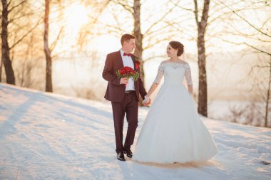 Bir gelin ve damat karda yürüyorlar, el ele tutuşuyorlar ve düğün kıyafetleri giyiyorlar. Sahne huzurlu ve romantik. Çiftler özel günlerinin tadını çıkarıyorlar.