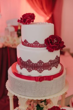 Üzerinde kırmızı çiçekler ve dantel olan iki katlı bir pasta. Pasta gümüş bir standa konur.
