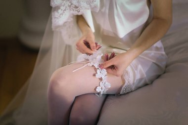 Gelinlik giymiş bir kadın bir yatakta oturuyor ve düğün trenini tamir ediyor. Gelin özel gününe hazırlanırken, zarafet ve entelektüellik kavramı