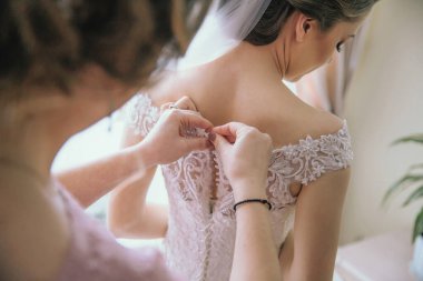 Bir kadın elbisesini bir kadın değiştiriyor. Gelin, dantel yakalı beyaz bir elbise giyiyor.