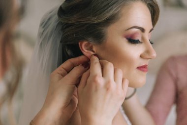 Bir kadın bir erkek tarafından kulaklarını deldiriyor. Kadın kırmızı bir elbise giyiyor ve kırmızı ruju var.