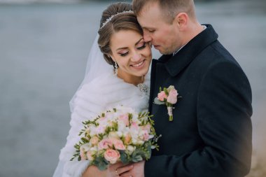 Gelin ve damat, gelinin elinde bir buket çiçekle birbirlerine sarılıyorlar.