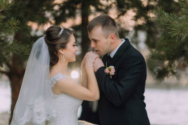 Bir gelin ve damat ormanda el ele tutuşuyorlar. Gelin beyaz bir elbise giyiyor ve damat siyah bir takım giyiyor.