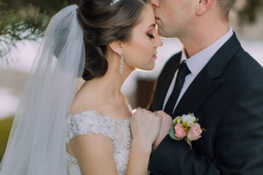 Bir gelin ve damat birbirlerinin dudaklarını öpüyor. Gelin beyaz bir peçe takıyor ve damat siyah bir takım giyiyor.