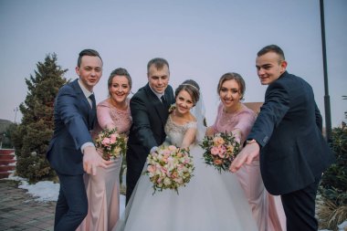 Bir grup insan bir resim için poz veriyor, bir gelin ve damat da dahil. Gelin bir buket çiçek tutuyor ve damat da bir buket çiçek tutuyor. Grup gülümsüyor.