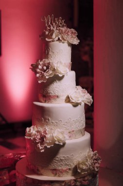 Beyaz kremalı ve pembe çiçekli dört katlı bir düğün pastası. Pasta altın harflerle süslenmiştir.