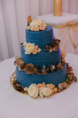 Üzerinde çiçekler olan mavi bir pasta. Pasta üç katlı ve altın kaplama. Çiçekler sarı ve turuncu.