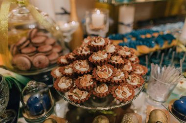 Çeşitli tatlılarla dolu bir masa, büyük bir yığın kahverengi kurabiye de dahil. Masa bir parti ya da toplantı için hazırlanır ve tatlılar görsel olarak çekici bir şekilde düzenlenir.