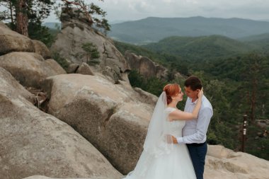 Gelin ve damat kayalık bir dağın tepesinde duruyorlar, gelin beyaz bir elbise ve damat mavi bir takım elbise giyiyor. Birbirlerini kucaklıyorlar ve sahnenin romantik bir yanı var.