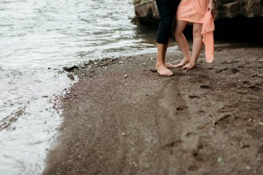 Kumsalda ayakları kuma basmış bir çift. Kadın turuncu bir elbise giyiyor.