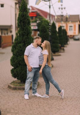 Ağacın önünde öpüşen bir çift. Adam beyaz gömlek ve kot pantolon giyiyor.