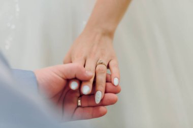 Kadının parmağında yüzük olan bir çift el ele tutuşuyor. Yüzük altın ve ortasında bir elmas var. Sahne romantik ve samimi.