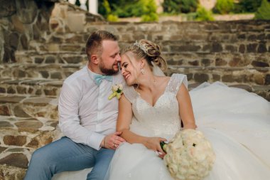 Gelin ve damat taş bir merdivende oturuyor, gelin bir buket tutuyor. Sahne mutlu ve romantik.