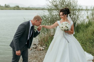 Bir erkek bir buket çiçek tutarken bir kadının elini öper. Sahne bir su kütlesi tarafından çekiliyor ve çift bir anlık yakınlığın tadını çıkarıyor gibi görünüyor.