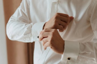 Bir adam beyaz gömlek giyiyor ve manşetlerini düzeltiyor. Formalite ve detaylara dikkat etme kavramı. Çünkü adam düzgün giyinmeye özen gösteriyor.