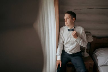 Takım elbiseli ve kravatlı bir adam pencerenin önünde oturmuş kravatını düzeltiyor. Formalite ve profesyonellik kavramı. Çünkü adam takım elbise ve kravat giymiş.