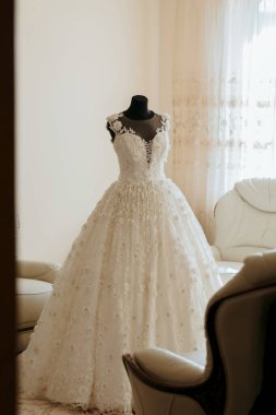 Üzerinde çiçekler olan beyaz bir elbise bir odada sergilenir. Elbise bir mankenin üzerinde asılı ve ilgi odağı. Odada bir kanepe ve bir sandalye var, ve perdeli bir pencere var.