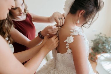 Üç kadın düğün için hazırlanıyor. Bir tanesi gelinin elbisesini ayarlıyor.