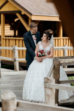 Gelin ve damat köprüde, gelin elinde buket tutuyor. Sahne romantik ve mutlu.