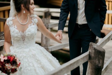 Bir gelin ve damat ahşap bir çitin yanında duruyor. Gelin beyaz bir elbise giyiyor ve damat bir takım elbise giyiyor. El ele tutuşup kameraya gülümsüyorlar. Sahne mutlu ve neşeli.