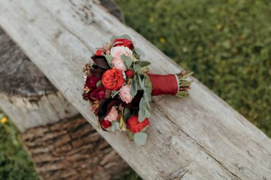 Tahta bir bankta duran bir buket kırmızı çiçek. Çiçekler bir denge ve uyum hissi yaratacak şekilde düzenlenmiştir. Bankın kendisi ahşaptan yapılmıştır ve kırsal, doğal bir hissi vardır.