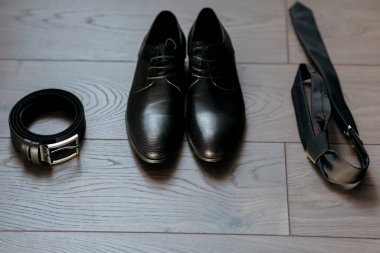 Bir çift siyah ayakkabı ve bir kemer ahşap bir zeminde. Ayakkabılar kemerin önüne konur ve kemer yerde asılı durur. Organizasyon ve hazırlık kavramı, ayakkabılar gibi