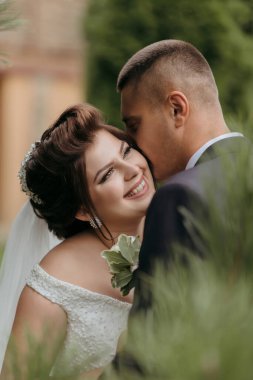 Bir gelin ve damat çimlerin üzerinde öpüşüyor. Gelin beyaz bir elbise giyiyor ve damat da takım elbise giyiyor.