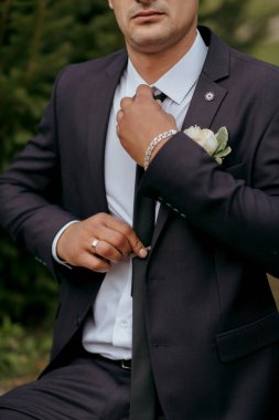 Takım elbiseli bir adam kravatını bağlamaya hazırlanıyor. Alyans ve saat takıyor.