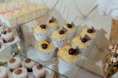 Üzerinde meyveli kekler olan çeşitli tatlılar içeren bir masa. Tatlılar cam bir yüzeye dizilmiştir ve çeşitli pasta ve hamur işleri vardır.