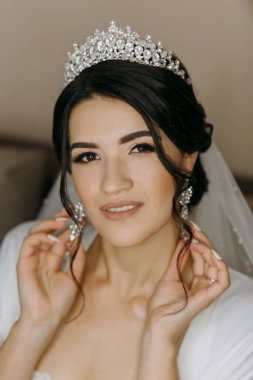 Kafasında taç olan bir kadın resim için poz veriyor. Beyaz bir elbise giyiyor ve elleri kalçasının üzerinde. Zarafet ve incelik kavramı