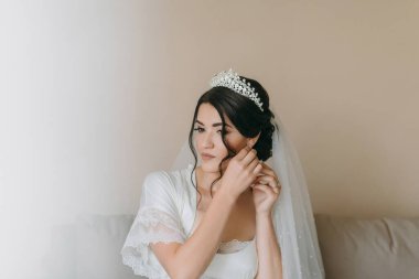 Bir kadın düğünü için hazırlanıyor ve tacını takıyor. Kanepede oturuyor ve aynada kendine bakıyor.