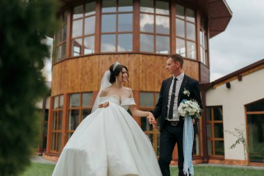 Bir gelin ve damat büyük bir binanın önünde bir patikadan aşağı yürüyorlar. Gelin beyaz bir elbise giyiyor ve damat bir takım elbise giyiyor. El ele tutuşuyorlar ve mutlu ve aşık görünüyorlar.