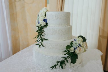 Üzerinde mavi çiçekler ve beyaz çiçekler olan beyaz bir düğün pastası. Pasta mavi kurdele ve beyaz kurdeleyle süslenmiş.