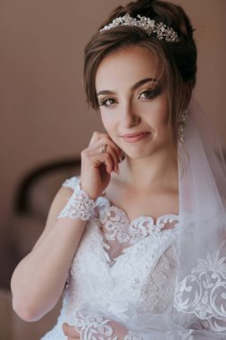 Beyaz gelinlik ve taç giyen bir kadın. Gülümsüyor ve kameraya bakıyor.