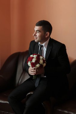 Takım elbiseli ve kravatlı bir adam bir buket kırmızı ve beyaz gül tutuyor. O bir kanepede oturuyor, kameraya bakıyor. Zarafet ve incelik kavramı