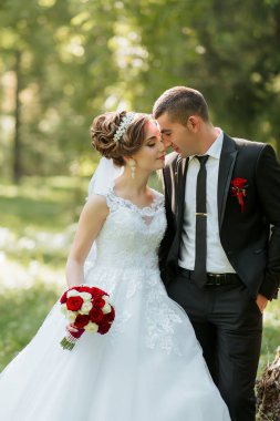 Gelin ve damat bir tarlada duruyorlar, gelin beyaz bir elbise giyiyor ve damat siyah bir takım elbise giyiyor. Gelin elinde bir buket kırmızı gül tutuyor ve damat kırmızı bir kravat takıyor.