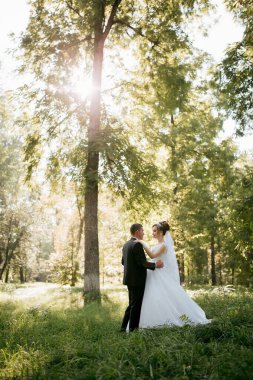 Bir gelin ve damat çimenli bir tarlada bir ağacın altında duruyor. Gelin beyaz bir elbise giyiyor ve damat bir takım elbise giyiyor. İkisi de gülümsüyor ve kameraya bakıyor.